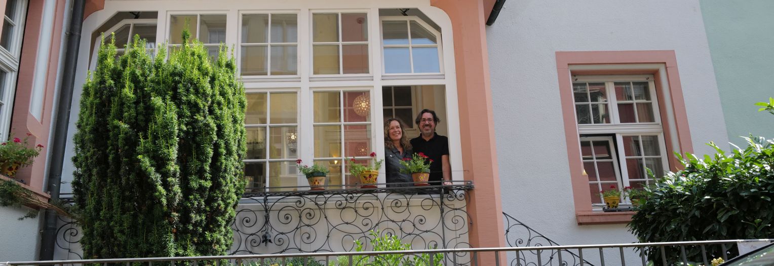 Chef und Chefin blicken aus dem Fenster, davor Büsche und Geländer sichtbar